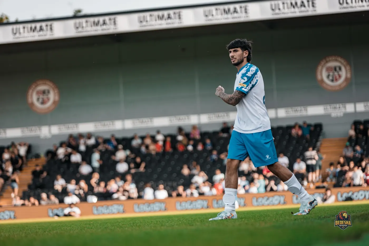 A player walking out at a football ground with LOGODY. advertising boards along the pitch